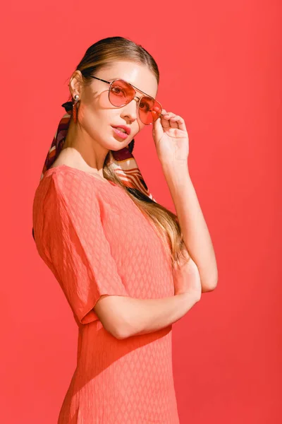 Modèle à la mode posant en robe de corail vivant et lunettes de soleil sur fond rouge — Photo de stock