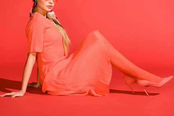 Обрезанный вид стильной девушки, позирующей в живом коралловом платье на красном фоне — стоковое фото