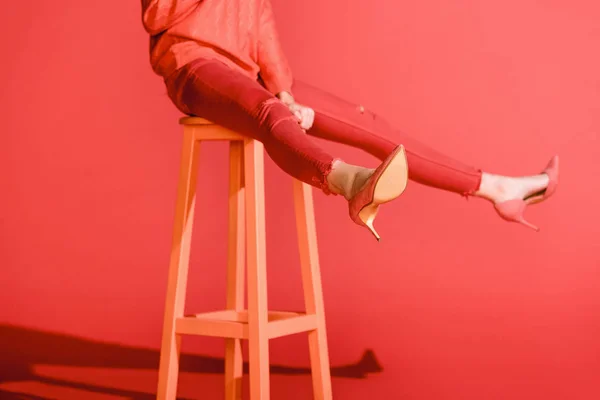 Vista ritagliata della ragazza alla moda in posa in abiti di corallo vivente su sgabello su sfondo rosso — Foto stock