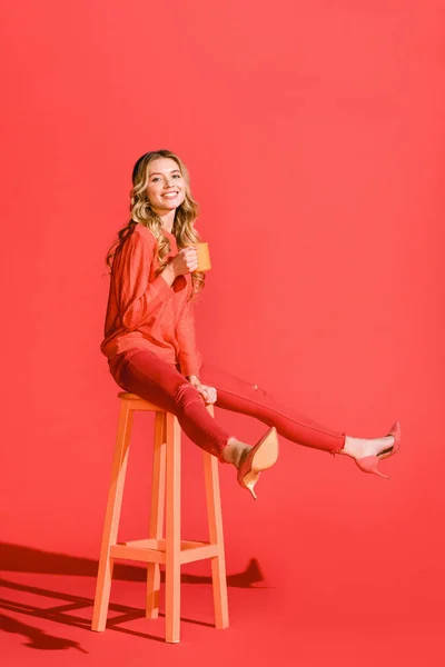 Happy stylish girl with cup of coffee sitting on stool on living coral. Pantone color of the year 2019 concept — Stock Photo