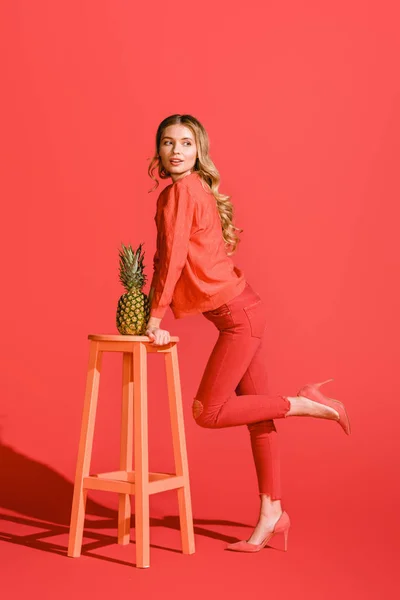Fashionable beautiful woman posing with pineapple at stool on living coral — Stock Photo