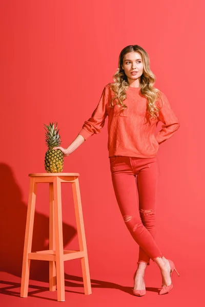 Stylish beautiful woman holding fresh pineapple at stool on living coral — Stock Photo