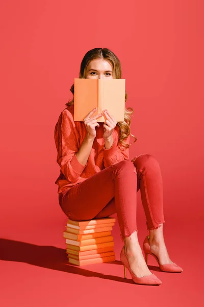 Fashionable girl reading book while sitting on books on living coral. Pantone color of the year 2019 concept — Stock Photo