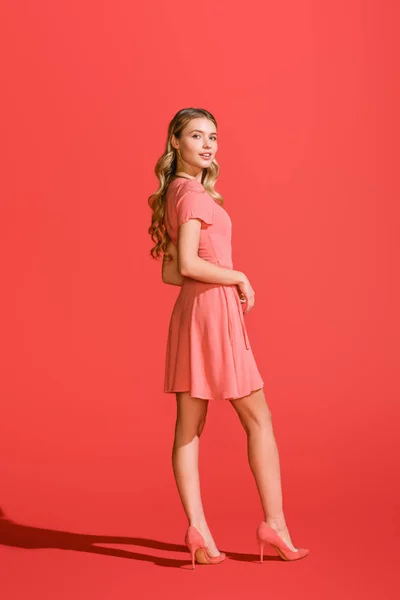 Chica rubia elegante posando en vestido de coral vivo sobre fondo rojo - foto de stock