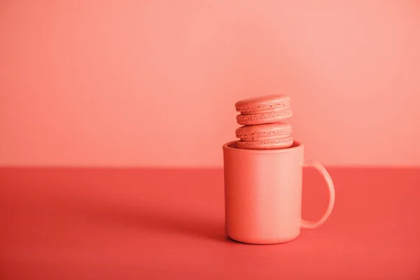 Macaroons doces na xícara no fundo coral vivo. Pantone cor do ano 2019 conceito — Fotografia de Stock