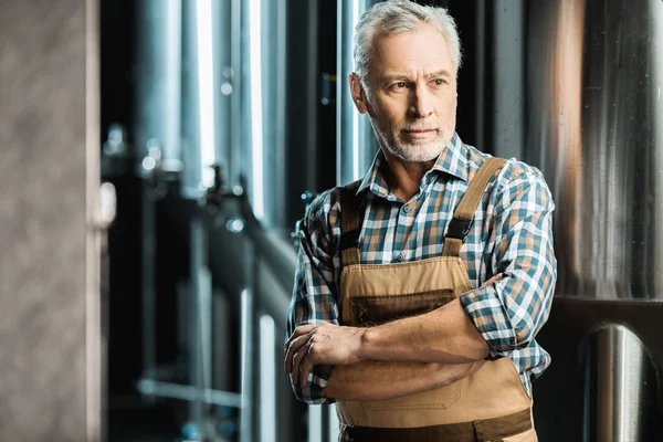 Braumeister posiert mit verschränkten Armen in Arbeitshose in Brauerei — Stockfoto