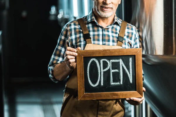 Cropped view of successful owner holding board with open sign in brewery — Stock Photo