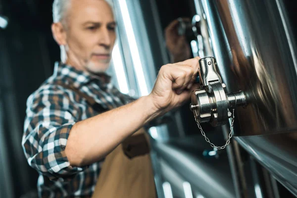 Enfoque selectivo de cervecero macho senior que trabaja con el equipo de la cervecería - foto de stock