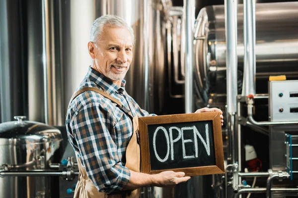 Smiling senior owner holding board with open sign in brewery — Stock Photo