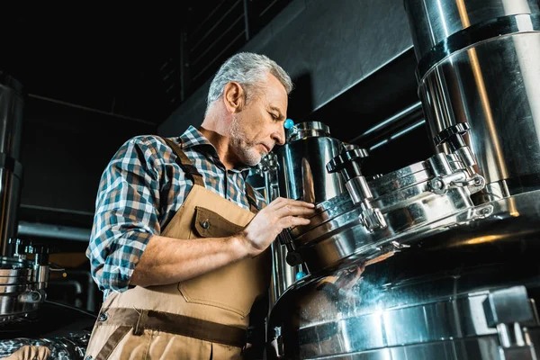 Brasseur professionnel senior en salopette travaillant avec du matériel de brasserie — Photo de stock