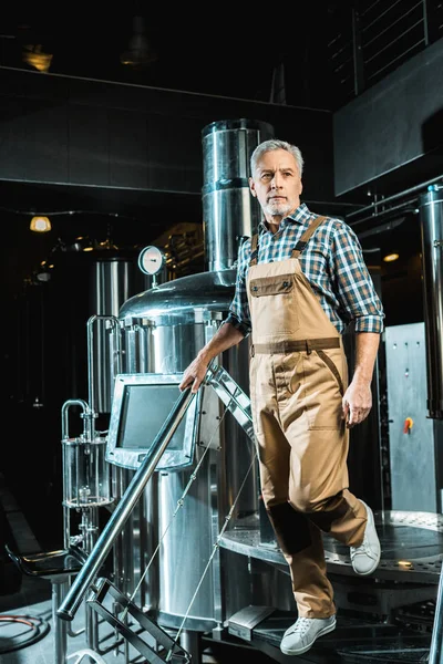 Professional senior brewer in overalls standing in brewery — Stock Photo