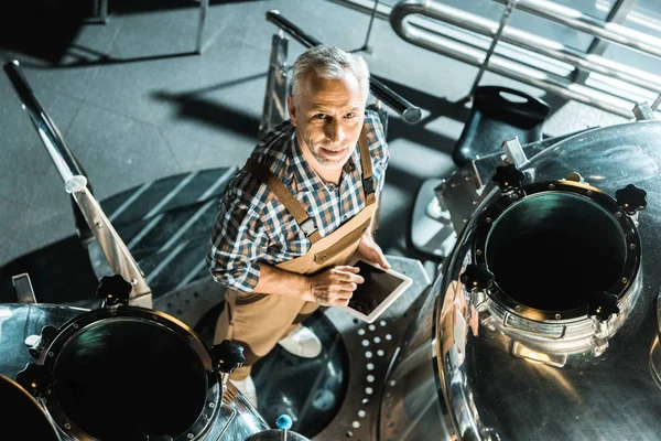 Overhead view of handsome male brewer using digital tablet in brewery — Stock Photo