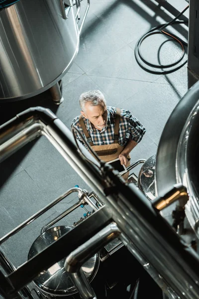 Вид зверху чоловіка старшого пивовара з використанням цифрового пристрою в пивоварні — стокове фото
