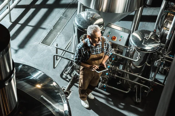 Visão aérea do cervejeiro no macacão de trabalho usando tablet digital na cervejaria — Fotografia de Stock