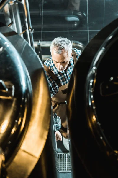 Вид сверху на профессионального пивовара в комбинезоне, работающего с пивоваренным оборудованием — стоковое фото