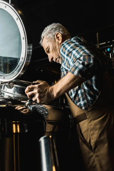 Braumeister in Arbeitskleidung überprüft Brauereiausrüstung — Stockfoto