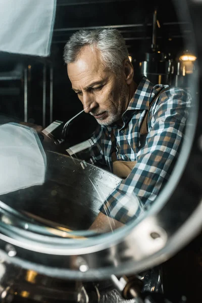 Cervejeiro macho sênior em macacões de trabalho verificando equipamentos cervejaria — Fotografia de Stock