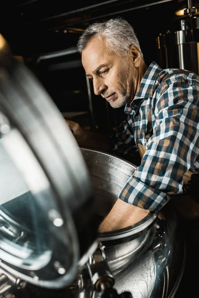 Cervejeiro macho profissional em macacões de trabalho inspecionando equipamentos cervejaria — Fotografia de Stock