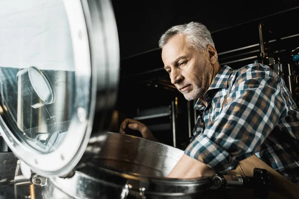 Професійний старший пивовар у робочому комбінезоні, що перевіряє пивоварне обладнання — стокове фото