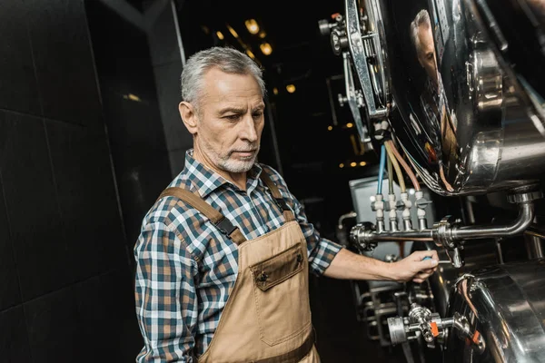 Professional male brewer in overalls working with brewery equipment — Stock Photo