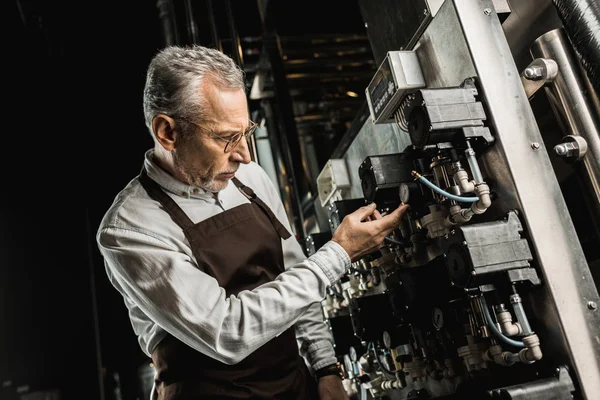 Handsome senior brewer in apron checking brewery equipment — Stock Photo