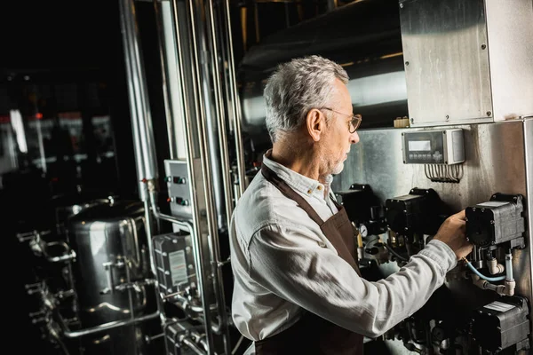 Bello birraio maschio in grembiule guardando attrezzature birreria — Foto stock