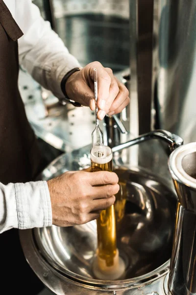 Обрезанный вид мужского пивовара, рассматривающего пиво во фляжке на пивоварне — стоковое фото