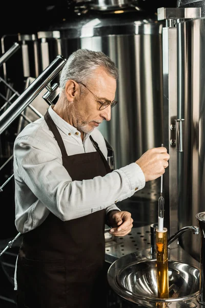 Birraio maschio professionista che esamina birra in fiaschetta in birreria — Foto stock