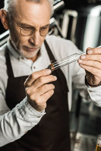 Selective focus of senior brewer examining beer in flask in brewery — Stock Photo