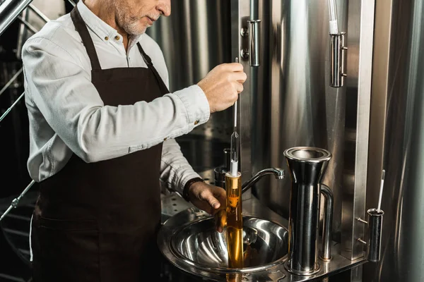 Ausgeschnittene Ansicht eines leitenden Brauers, der Bier im Kolben in der Brauerei untersucht — Stockfoto