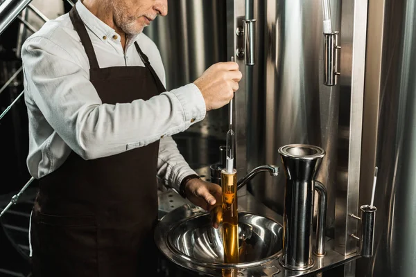 Vista cortada de cervejeiro sênior examinando cerveja em frasco na cervejaria — Fotografia de Stock