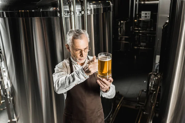 Senior brewer looking at glass of beer in brewery — Stock Photo