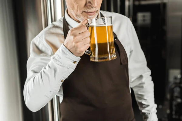 Cropped view of senior owner testing beer in brewery — Stock Photo
