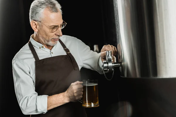 Senior male brewer pouring beer into glass in brewery — Stock Photo