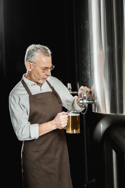 Cervejeiro sênior bonito derramando cerveja para testes na cervejaria — Fotografia de Stock