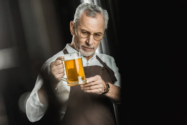Professional brewer looking at glass of beer in brewery — Stock Photo
