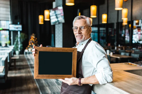 Sorridente proprietário de pub segurando placa vazia e de pé perto bar contador — Fotografia de Stock