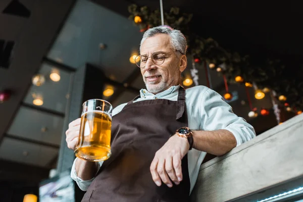 Trabalhador masculino no avental segurando vidro de cerveja no pub — Fotografia de Stock