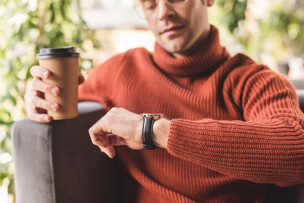 Selective focus of pensive man holding paper cup while looking at watch in cafe — Stock Photo