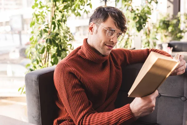 Красивый мужчина в очках, читающий книгу, сидя в кафе — стоковое фото