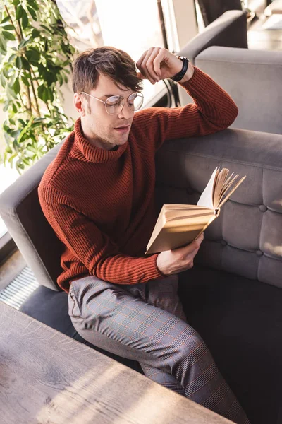 Nachdenklicher Mann mit Brille liest Buch, während er im Café sitzt — Stockfoto