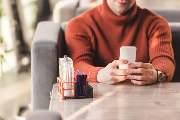 Vista recortada del hombre usando teléfono inteligente cerca de botellas de vidrio con sal y papel en la cafetería - foto de stock