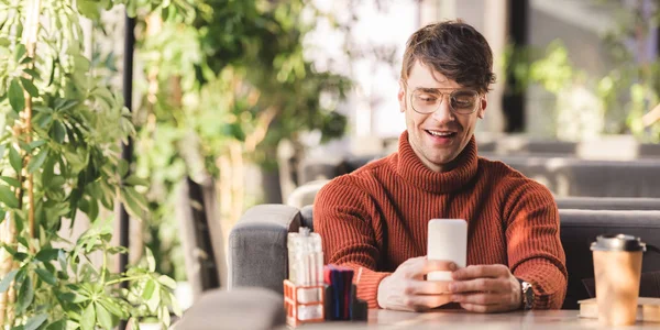 Homme souriant en utilisant smartphone près de tasse jetable dans le café — Photo de stock