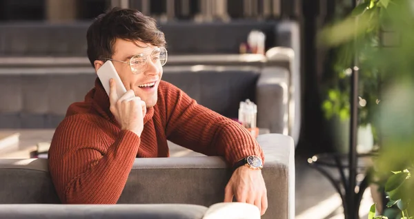 Homme souriant parlant sur smartphone tout en étant assis dans le café — Photo de stock