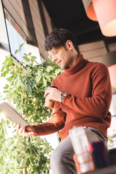 Homme heureux dans des lunettes regardant ordinateur portable et tenant tasse jetable dans le café — Photo de stock