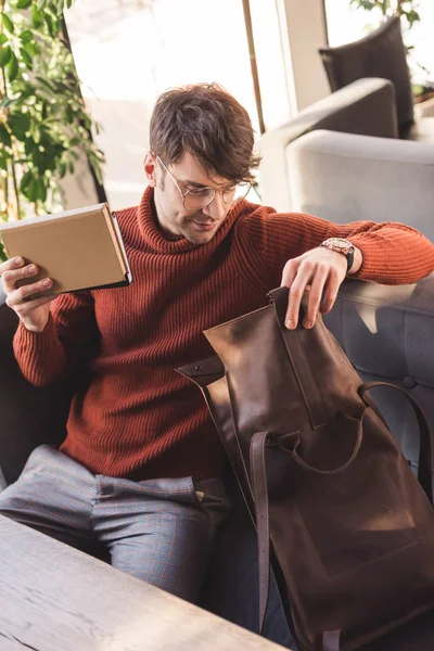 Homme gai dans des lunettes tenant des livres et regardant sac dans le café — Photo de stock