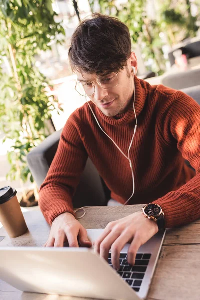 Hombre alegre escuchar música en los auriculares mientras se utiliza el ordenador portátil en la cafetería - foto de stock