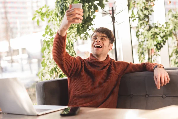 Sorrindo homem em óculos tomando selfie perto de laptop no café — Fotografia de Stock