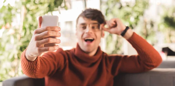 Selective focus of man holding smartphone while taking selfie in cafe — Stock Photo