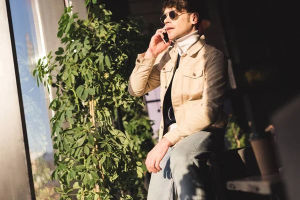 Hombre guapo y elegante en gafas de sol hablando en el teléfono inteligente - foto de stock